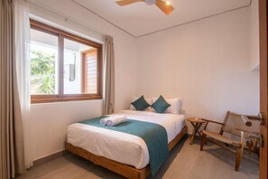 Ein Schlafzimmer mit Bett, Fenster, Deckenventilator und Stuhl.