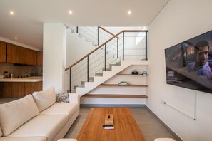 Ein modernes Wohnzimmer mit Treppe, einem flachbildfernseher an der Wand und einem Holztisch.