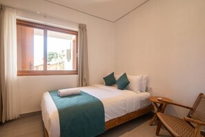 A single bed with a wooden frame, a small bedside table, a wicker chair, and a window with curtains. - Private 3BR Villa Uluwatu 5 Mins to Beach (Pecatu)