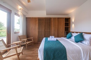 Quarto de hotel com cama, uma cadeira, um guarda-roupa de madeira e uma janela.