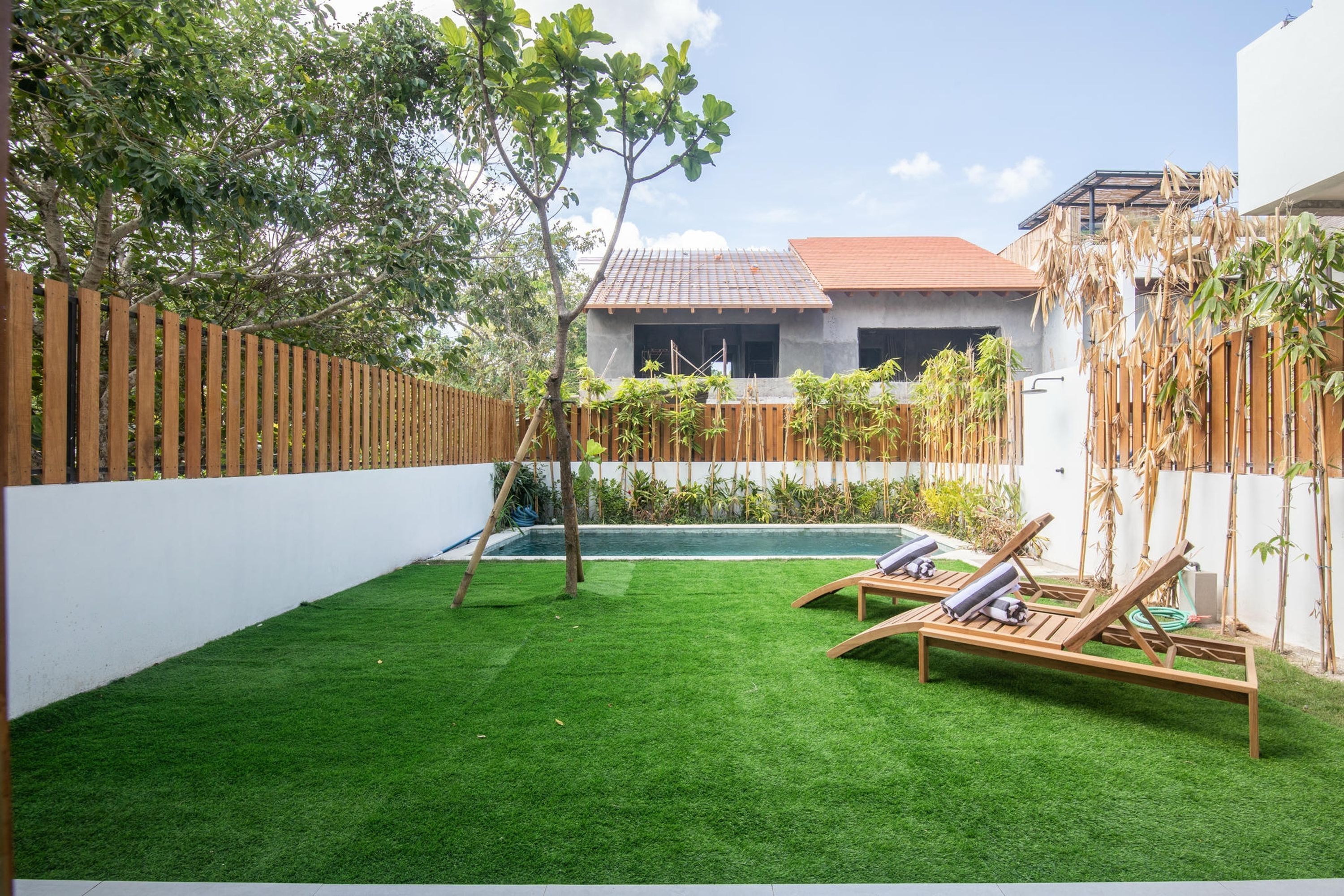 Um quintal com grama sintética, uma piscina e duas espreguiçadeiras.