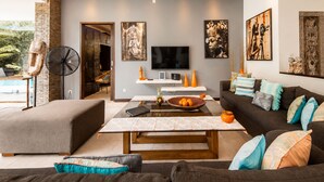 Ein modernes Wohnzimmer mit Flachbildfernseher, Couchtisch und Sofa. Ein Ventilator und ein dekoratives Wandbild sind ebenfalls vorhanden.