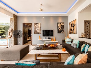 Ein modernes Wohnzimmer mit Flachbildfernseher, Couchtisch und Sofa. Ein Ventilator und ein dekoratives Wandbild sind ebenfalls vorhanden.