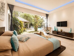 Ein modernes Schlafzimmer mit einem großen Bett, einem Fernseher und Blick auf ein Schwimmbad und einen Garten.
