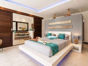 A modern bedroom with a large bed, a wardrobe, a mirror, and decorative wall art. - Rosa Paradise - Luxury 4BR Villa in Seminyak (Keroboken Kelod)