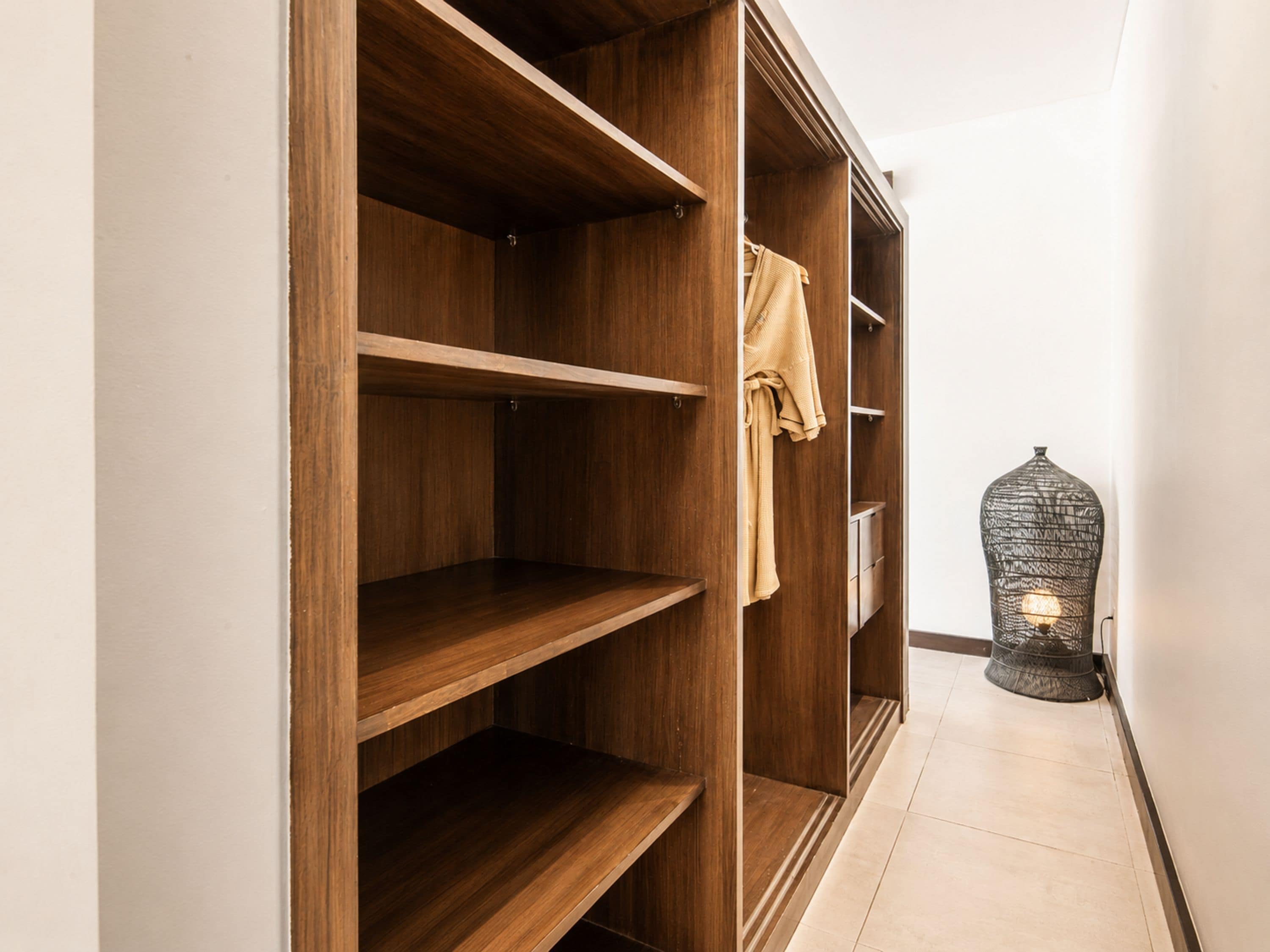 A wooden wardrobe with multiple shelves and a hanging rod, a light fixture, and a tiled floor.