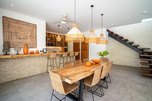 Une cuisine moderne avec une table à manger en bois, des chaises en osier et des luminaires suspendus.