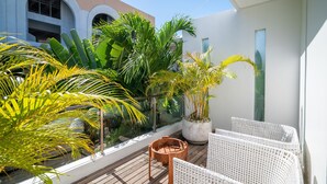 A balcony with potted plants, wicker furniture, and a view of a building with arched windows. - Modern Coastal 4BR Villa Walk to Finns Canggu (Tibubeneng)