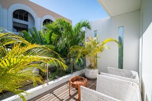 A balcony with potted plants, wicker furniture, and a view of a building with arched windows. - Modern Coastal 4BR Villa Walk to Finns Canggu (Tibubeneng)