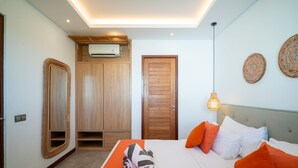 A hotel room with a bed, a wooden wardrobe, a mirror, an air conditioning unit, and decorative wall plates. - Modern Coastal 4BR Villa Walk to Finns Canggu (Tibubeneng)