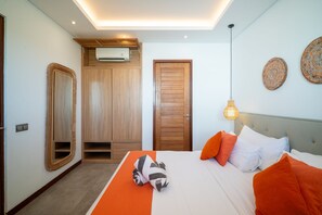 A hotel room with a bed, a wooden wardrobe, a mirror, an air conditioning unit, and decorative wall plates. - Modern Coastal 4BR Villa Walk to Finns Canggu (Tibubeneng)
