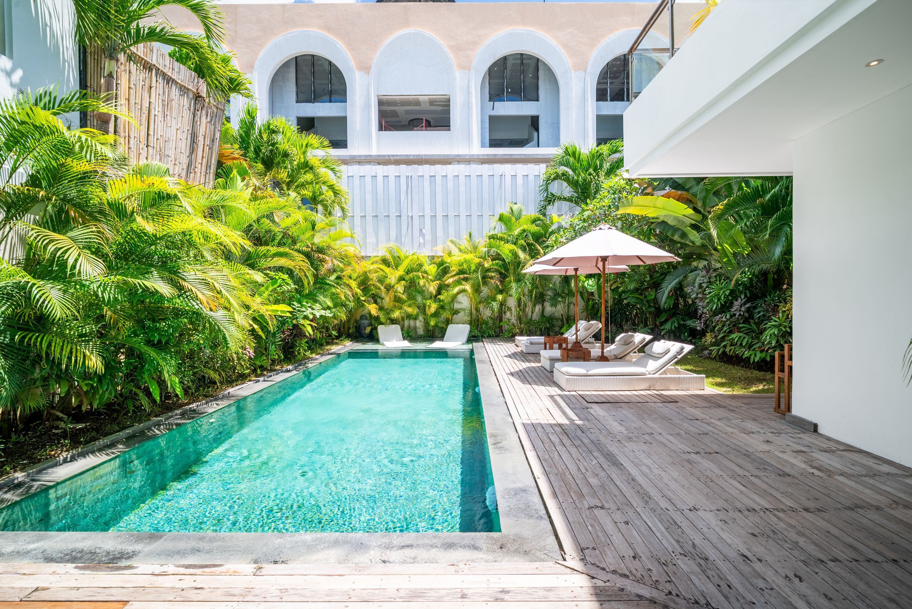 A swimming pool with clear water, surrounded by lush greenery and a wooden deck.