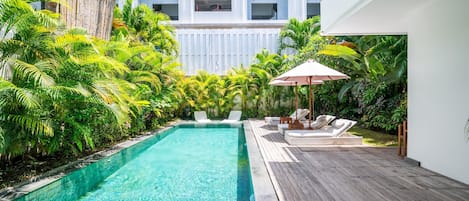 A swimming pool with clear water, surrounded by lush greenery and a wooden deck.