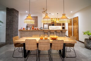 Ein moderner Essbereich mit Holztisch und Korbstühlen, im Hintergrund eine Küche und eine große Topfpflanze.