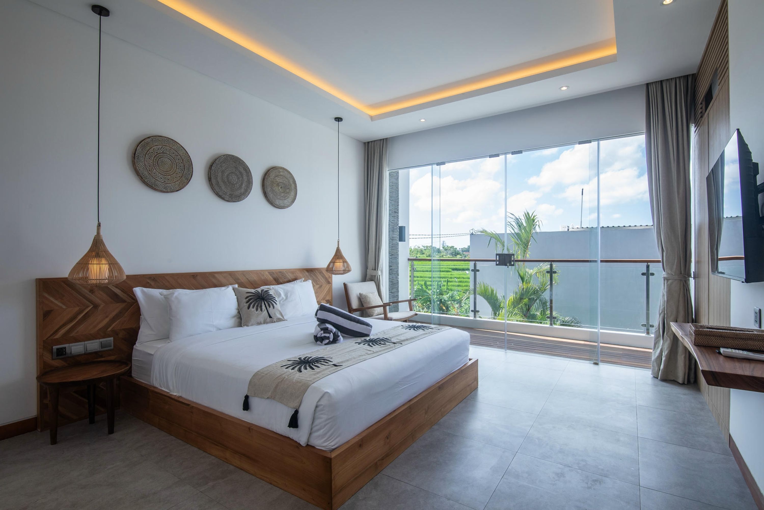 A modern bedroom with a large bed, bedside lamps, and a view of a green landscape through large windows.