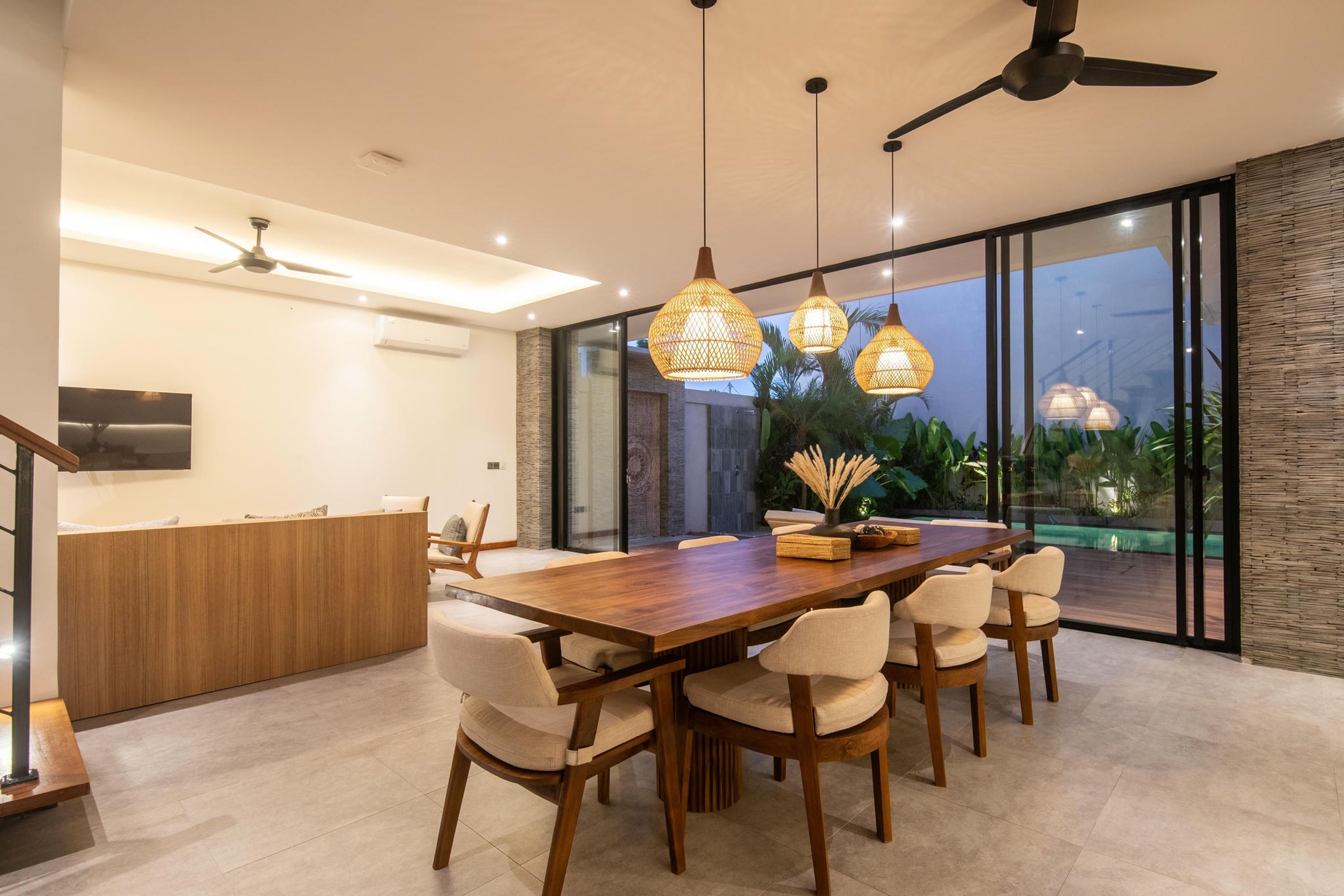 A modern dining area with a wooden table and chairs, pendant lighting, and a view of a swimming pool.