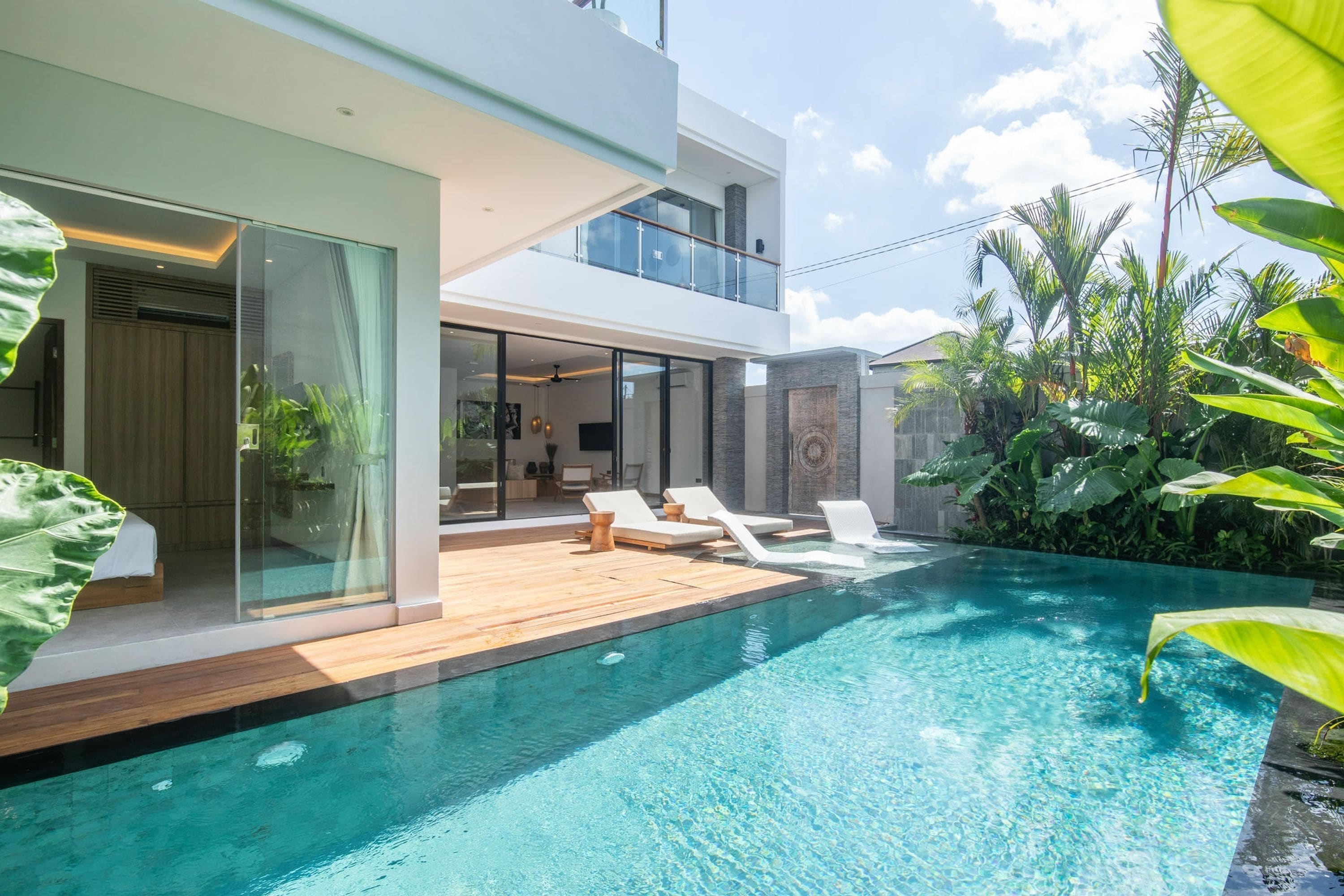 A modern house with a swimming pool, a balcony, and tropical plants.