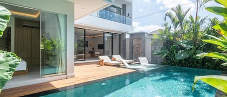 A modern house with a swimming pool, a balcony, and tropical plants.