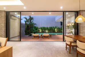 Ein modernes Interieur mit Glastür zum Poolbereich, Holzmöbeln und einem Esstisch.