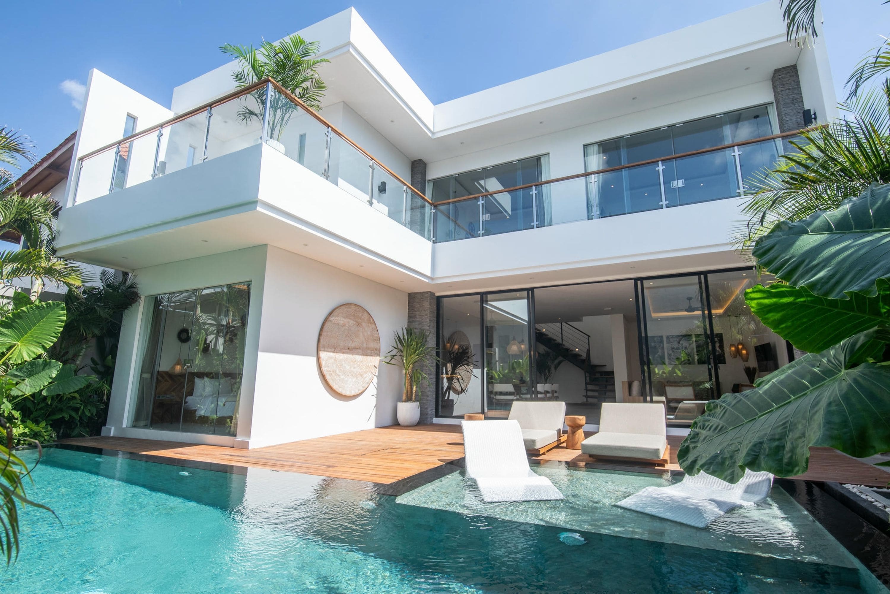 Ein modernes, zweistöckiges Haus mit einem Glasbalkon, einem Swimmingpool und tropischen Pflanzen.