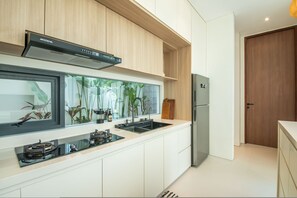 A modern kitchen with a built-in stove, a stainless steel refrigerator, and a window with a view of greenery. - Casa Rio-beautiful 3br Villa Center Seminyak (Keroboken Kelod)