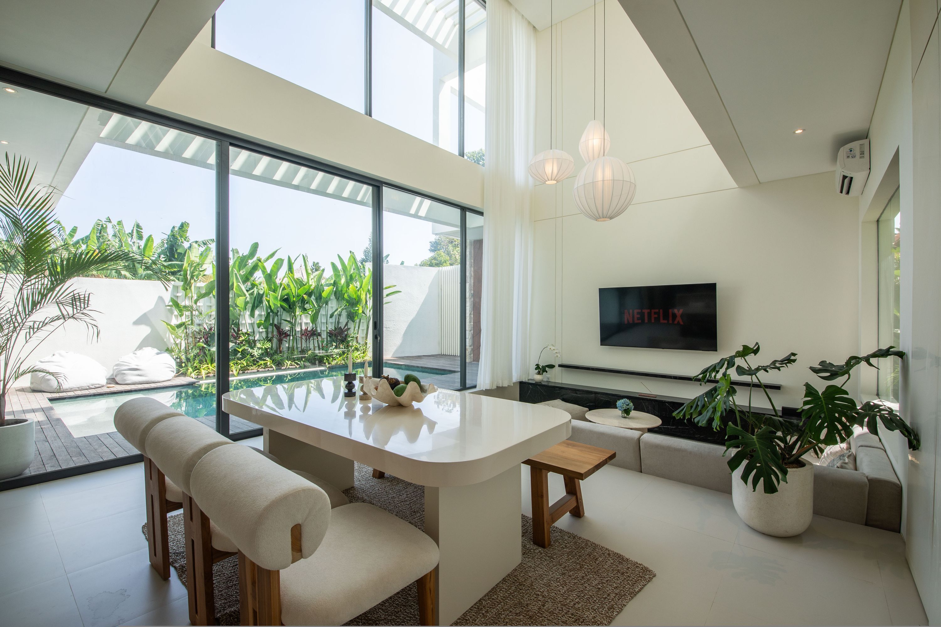A modern living room with a large TV, a pool view, and a dining area.