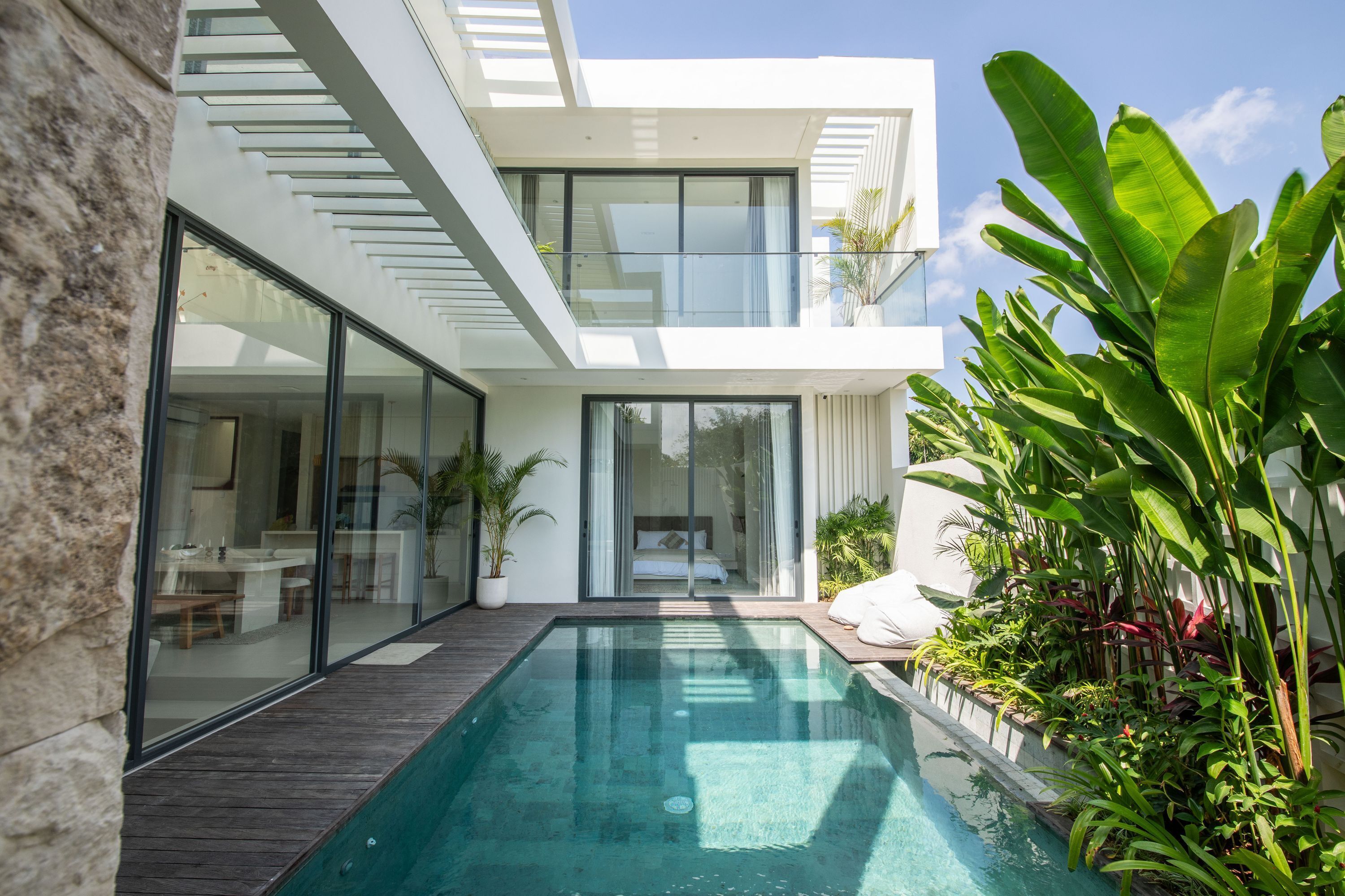 A modern two-story house with a glass facade, a wooden deck, and a swimming pool.