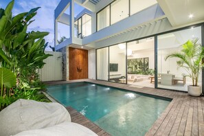 Ein modernes Haus mit Pool, einer Terrasse und Gartenmöbeln sowie eine große Glasdoor, die zu einem Innenbereich führt.