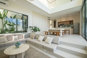 A modern living room with a sofa, coffee table, and a view of the kitchen. - Casa Rio-beautiful 3br Villa Center Seminyak (Keroboken Kelod)