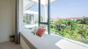 A modern room with a large window, a bed with pillows, and a view of a residential area. - Casa Rio-beautiful 3br Villa Center Seminyak (Keroboken Kelod)