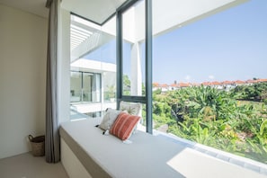 Ein modernes Zimmer mit großem Fenster, einem Bett mit Kissen und Blick auf eine Wohngegend.