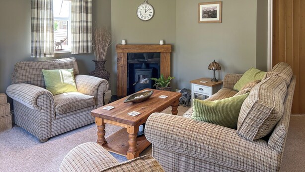 A living room with two sofas, a wooden coffee table, a fireplace, and a clock on the wall. - 3 bedroom accommodation in Beadnell (Beadnell)