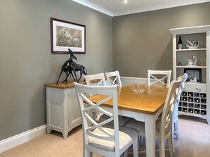 A dining area with a wooden table, white chairs, a white cabinet with wine bottles, and a framed picture on the wall. - 3 bedroom accommodation in Beadnell (Beadnell)
