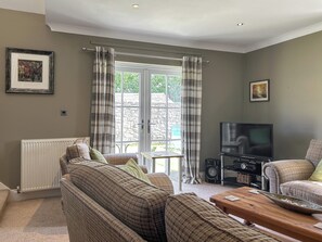 Ein Wohnzimmer mit einer Couch, einem Couchtisch, einem Fernseher und einem Fenster mit Vorhängen.