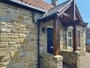 A stone building with a wooden porch and a door. - 3 bedroom accommodation in Beadnell (Beadnell)