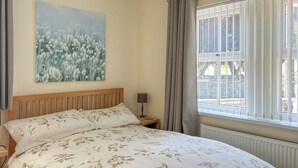 A bedroom with a bed, a nightstand, a lamp, a window with curtains, and a wall painting. - 3 bedroom accommodation in Beadnell (Beadnell)