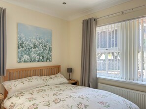 A bedroom with a bed, a nightstand, a lamp, a window with curtains, and a wall painting. - 3 bedroom accommodation in Beadnell (Beadnell)