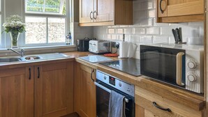 A kitchen with wooden cabinets, a built-in microwave, a toaster, and a window with a view of greenery. - 3 bedroom accommodation in Beadnell (Beadnell)