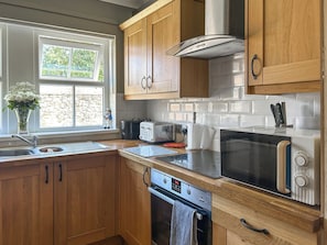 A kitchen with wooden cabinets, a built-in microwave, a toaster, and a window with a view of greenery. - 3 bedroom accommodation in Beadnell (Beadnell)