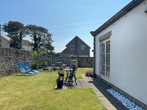 A backyard with a stone wall, a blue slide, a table with chairs, and a house with a stone facade. - 3 bedroom accommodation in Beadnell (Beadnell)