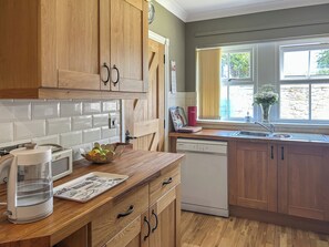 A kitchen with wooden cabinets, a dishwasher, a sink, and a window with curtains. - 3 bedroom accommodation in Beadnell (Beadnell)