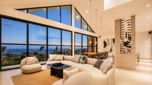 A modern living room with a large window, a sofa, a coffee table, and a dining area. - Modern 4 BR Villa Ocean View Nusa Dua (Nusa Dua)