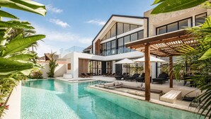 A modern house with a swimming pool, outdoor seating, and lush greenery. - Modern 4 BR Villa Ocean View Nusa Dua (Nusa Dua)
