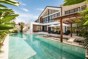 Ein modernes Haus mit Swimmingpool, Sitzgelegenheit im Freien und üppiger Bepflanzung.