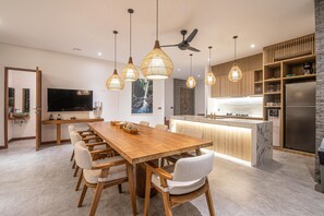 Eine moderne Küche mit Esstisch aus Holz, Pendelleuchten und einer integrierten Kochinsel.
