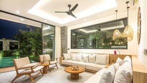 A modern living room with a large window, a ceiling fan, and a pool visible outside. - Modern 4br Villa Canggu Rice View AC (Tibubeneng)
