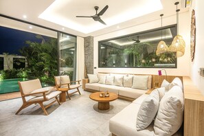 Ein modernes Wohnzimmer mit großem Fenster, Deckenventilator und Blick auf einen Pool.