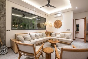 Ein modernes Wohnzimmer mit Ecksofa, Holzmöbeln, Pendelleuchten und einem großen Fenster.