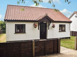 Een gelijkvloers huis met een pannendak, een houten omheining en een klein terras met bloembakken.
