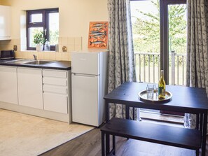 A kitchenette with a refrigerator, sink, and cabinets, a dining table with a tray holding glasses and a bottle, and a window with curtains. - 2 bedroom accommodation in Repps-with-Bastwick (Repps-with-Bastwick)